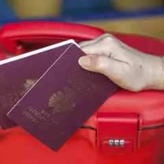 Dłoń trzyma polskie paszporty na czerwonej walizce. Kto może odebrać paszport osoby dorosłej? Tylko ona!