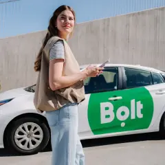 Kobieta z telefonem stoi obok białego samochodu Bolt z zielonym logo.