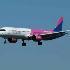Samolot Wizz Air z różowym i niebieskim ogonem zbliża się do lądowania. Wpisz "gdzie znalezc kod potwierdzenia wizzair" w wyszukiwarkę, aby znaleźć potrzebne informacje.