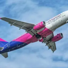 Samolot Wizz Air z różowo-niebieskim ogonem wznosi się na tle błękitnego nieba.