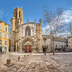 Katedra w Aix-en-Provence, z żółtą kamienicą obok, na brukowanym placu pod błękitnym niebem.