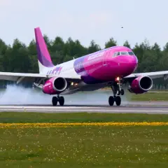 Różowy samolot Wizz Air ląduje na pasie startowym, unosząc dym.