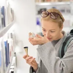 Kobieta z plecakiem wącha perfumy, zastanawiając się, ile kosztują perfumy na lotnisku.