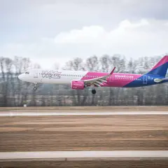 Samolot Wizz Air z różowym i niebieskim ogonem ląduje na pasie startowym.