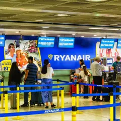 Kasa biletowa i punkty odprawy bagażu Ryanair na lotnisku, z ludźmi i bagażami.