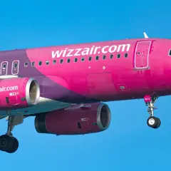 Różowy samolot Wizz Air z widocznymi silnikami i podwoziem na tle błękitnego nieba.