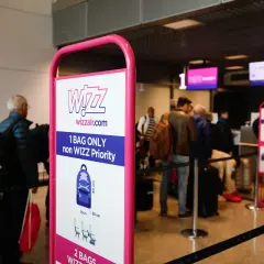 Tablica Wizzair z zasadami bagażu podręcznego, w tle kolejka pasażerów do odprawy.