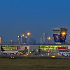 Lotnisko Chopina tętni życiem nocą, z samolotami na płycie i oświetlonymi budynkami.