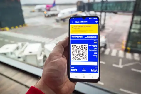 Smartfon z kartą pokładową Ryanair, pokazujący jak pobrać karty pokładowe Ryanair. Widok na lotnisko.