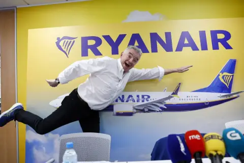 Michael O'Leary, znany jako właściciel Ryanaira, wesoło pozuje na tle samolotu i logo linii lotniczych.