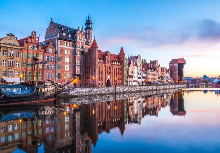 Zachód słońca nad Motławą w Gdańsku, z zabytkowymi kamieniczkami i żaglowcem. Idealne miejsce na podróż, gdy planujesz loty Wrocław Gdańsk.