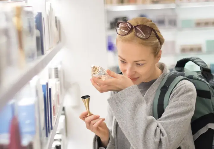 Kobieta z plecakiem wącha perfumy, zastanawiając się, ile kosztują perfumy na lotnisku.