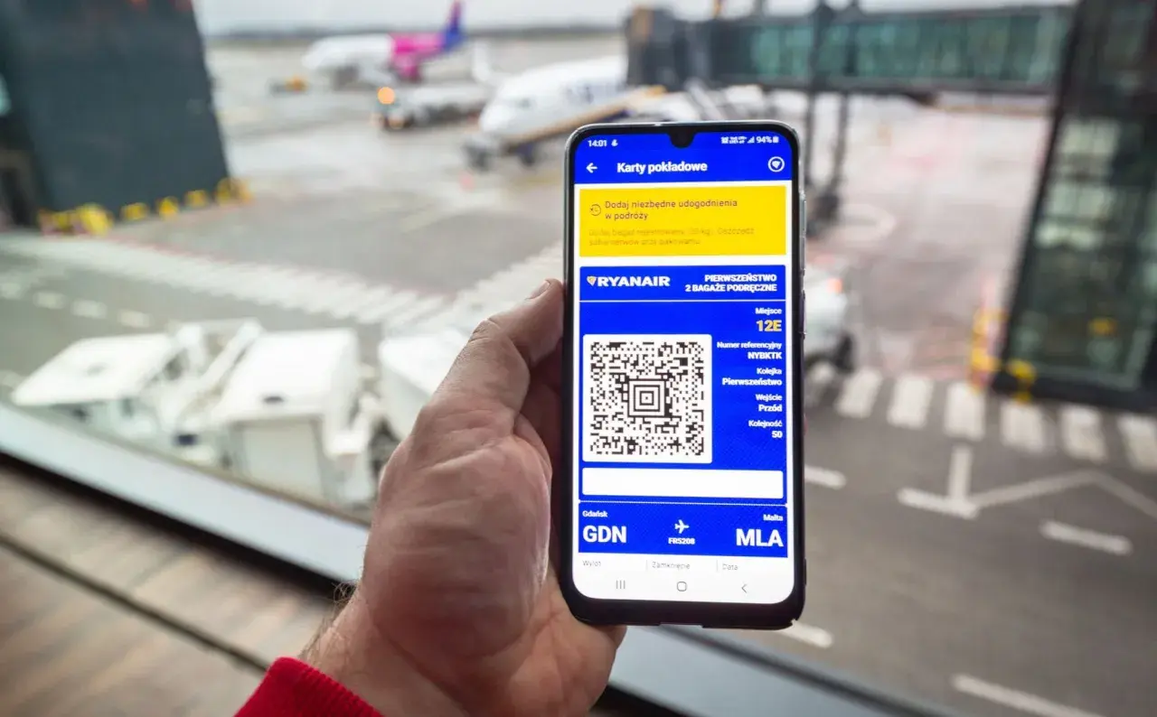 Smartfon z kartą pokładową Ryanair, pokazujący jak pobrać karty pokładowe Ryanair. Widok na lotnisko.