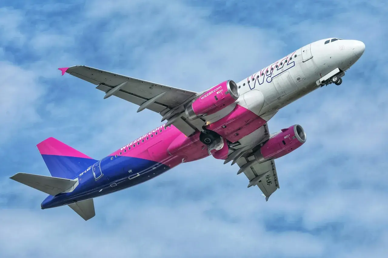 Samolot Wizz Air z różowo-niebieskim ogonem wznosi się na tle błękitnego nieba.