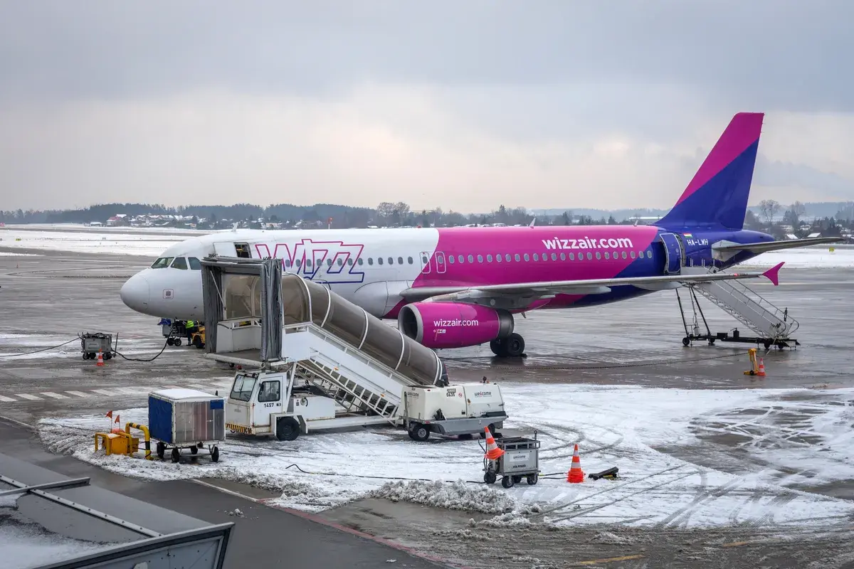 Samolot Wizz Air na lotnisku zimą, z drabiną i sprzętem naziemnym.