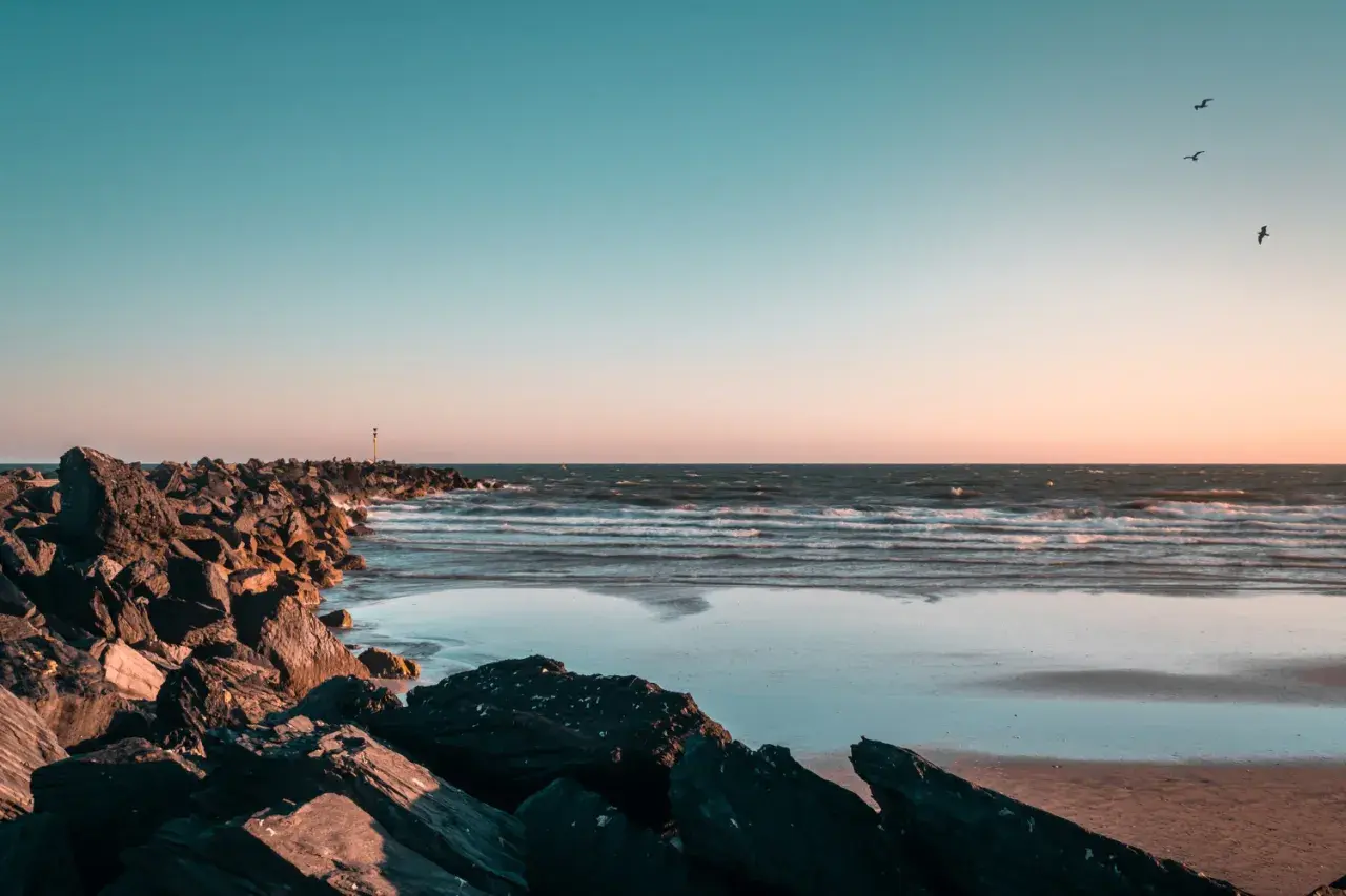 Kamienista plaża, fale i mewy na tle zachodzącego słońca. Idealne miejsce, kiedy jod nad morzem.