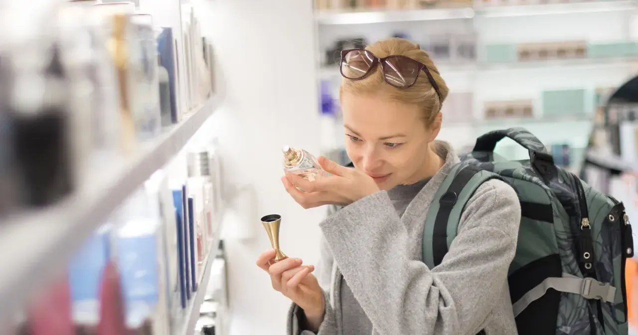 Kobieta z plecakiem wącha perfumy, zastanawiając się, ile kosztują perfumy na lotnisku.
