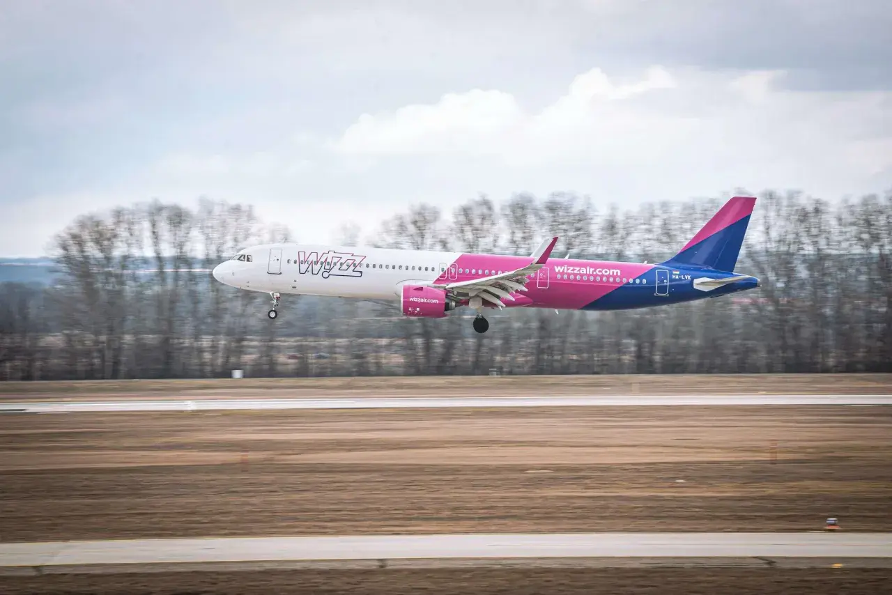 Samolot Wizz Air z różowym i niebieskim ogonem ląduje na pasie startowym.
