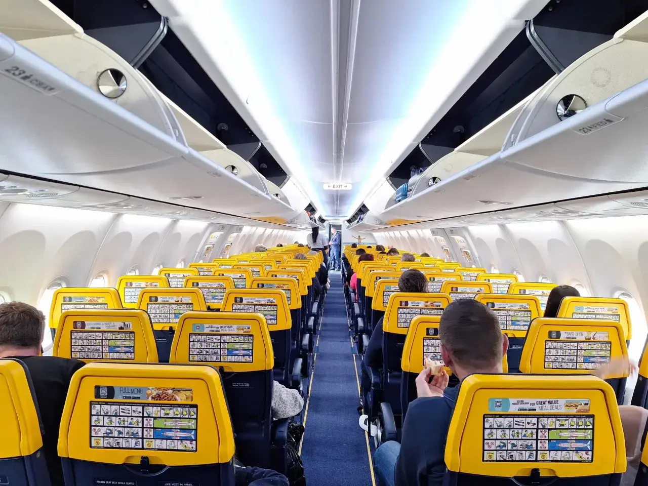 Wnętrze samolotu Ryanair z żółtymi zagłówkami. Na jednym z nich widoczna jest reklama "Great Value Meal Deals", która może pomóc w znalezieniu informacji, jak w aplikacji Ryanair zmienić walutę.