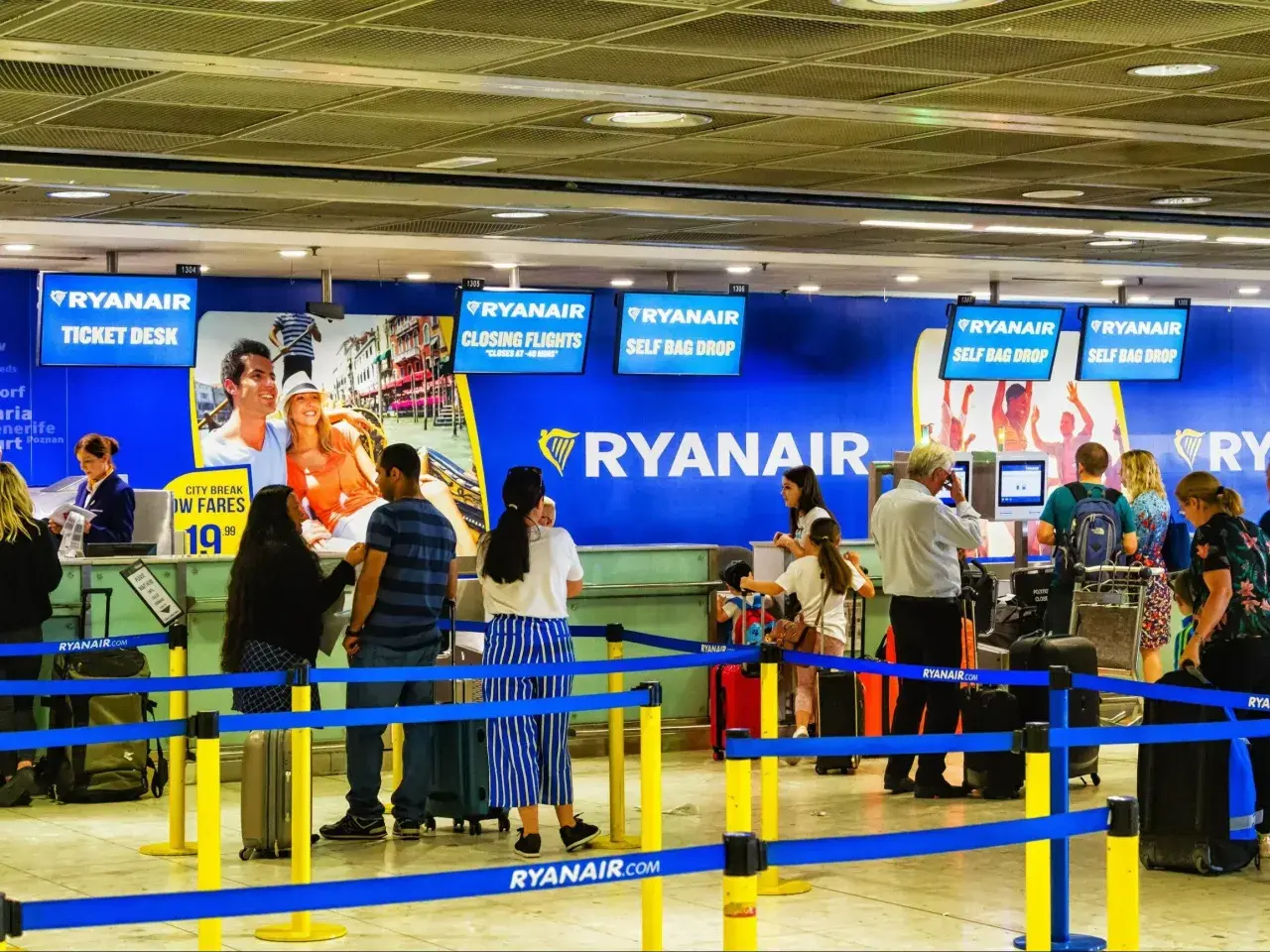 Kasa biletowa i punkty odprawy bagażu Ryanair na lotnisku, z ludźmi i bagażami.