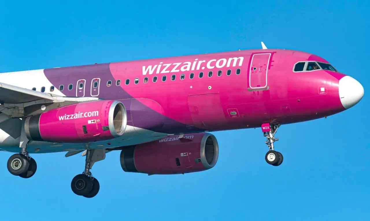 Różowy samolot Wizz Air z widocznymi silnikami i podwoziem na tle błękitnego nieba.