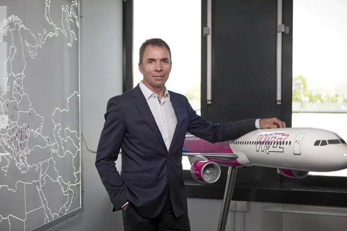 Mężczyzna w garniturze stoi obok modelu samolotu Wizz Air, z mapą Europy w tle.