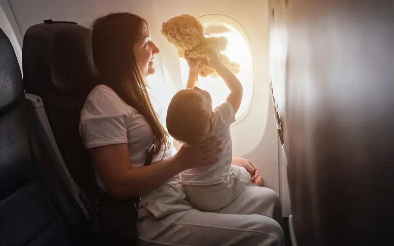 Mama z dzieckiem w samolocie, które bawi się misiem przy oknie. Warto wiedzieć, jak dodać dziecko do rezerwacji Ryanair.