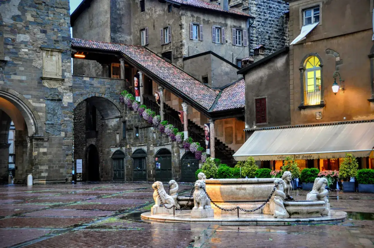 Urokliwy plac w Bergamo z kamienną fontanną i lwami. Idealne miejsce na rozpoczęcie podróży, gdy szukasz loty do Bergamo.