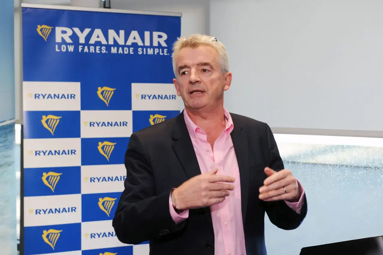 Michael O'Leary, znany jako właściciel Ryanaira, przemawia na tle niebieskiego banera z logo linii lotniczych.