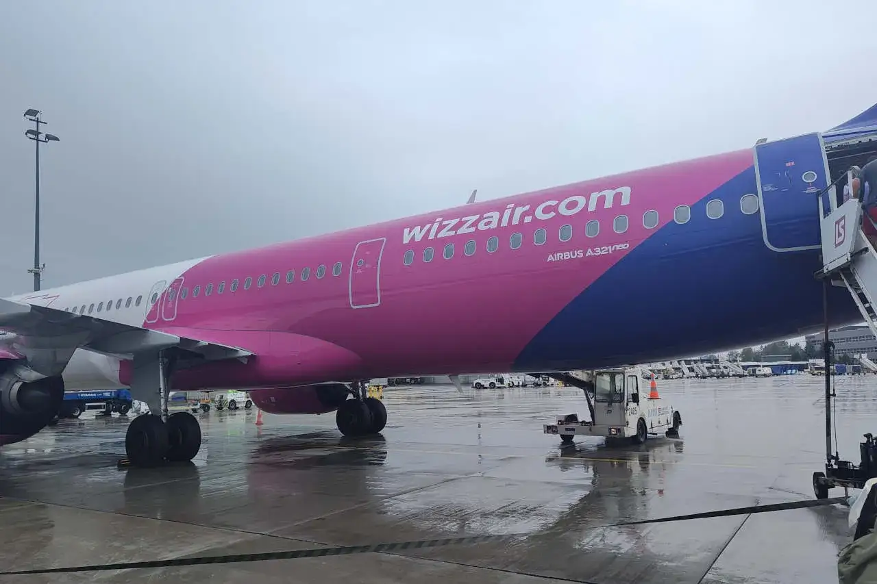 Różowy samolot Wizzair na płycie lotniska. Jeśli Twój lot został opóźniony lub odwołany, dowiedz się, jak złożyć wniosek o odszkodowanie Wizzair.