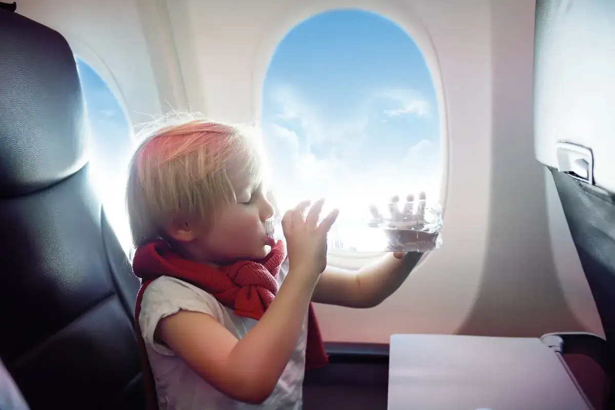 Chłopiec pije wodę w samolocie. Planujesz podróż i zastanawiasz się, jak dodać dziecko do rezerwacji Ryanair?